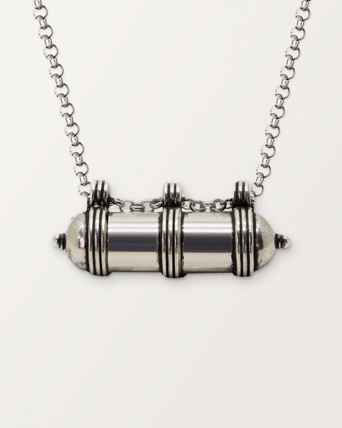 Close-up of the closed sterling silver Pankaj amulet necklace, with its three banded collars and bails, on a warm bone-white background.