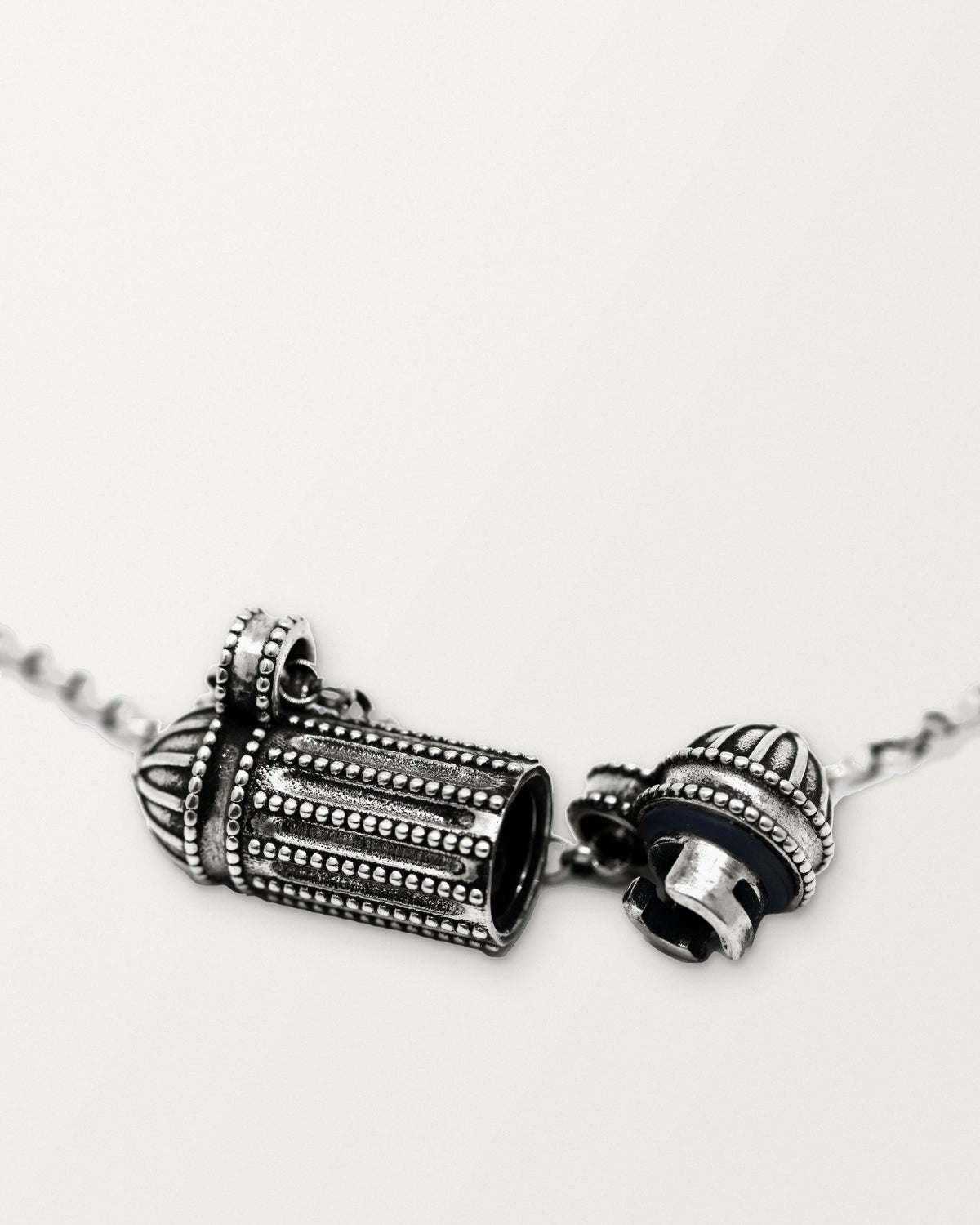 The sterling silver Taweez amulet necklace open, its cap still on the chain by its own bail, beside the hollow chamber.