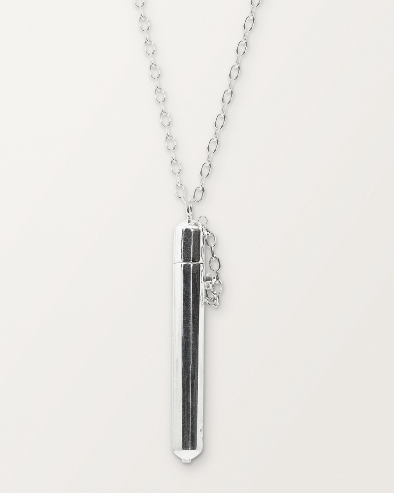 Sterling silver Moksha amulet necklace, closed, hanging on its chain against a warm bone-white background.