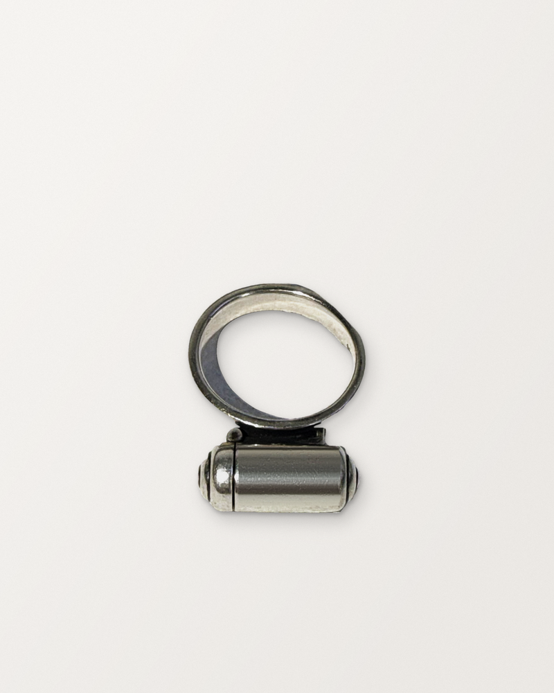 Sterling silver VRAT ring amulet, closed, on a warm bone-white background.