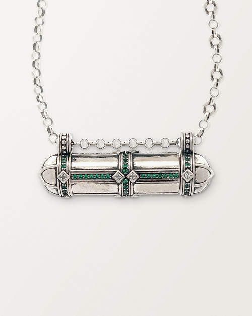 Close-up of the closed sterling silver Afghani Tribal Emerald amulet necklace, front, on a warm bone-white background.