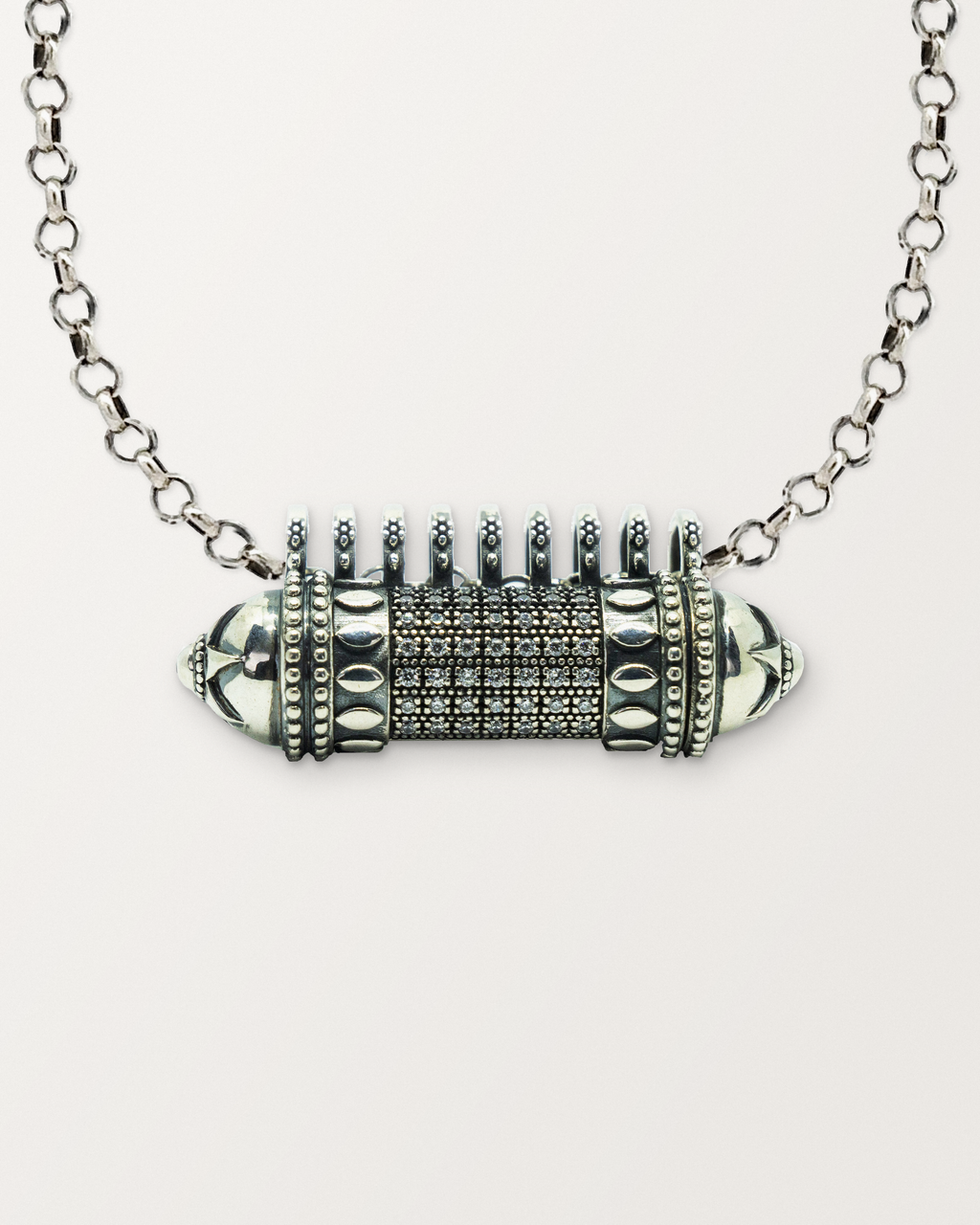 Close-up of the closed sterling silver Antique Pave amulet necklace, front, on a warm bone-white background.