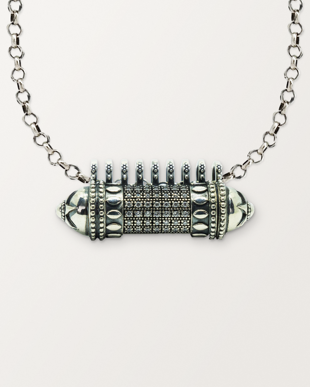 Close-up of the closed sterling silver Antique Pave amulet necklace, front, on a warm bone-white background.