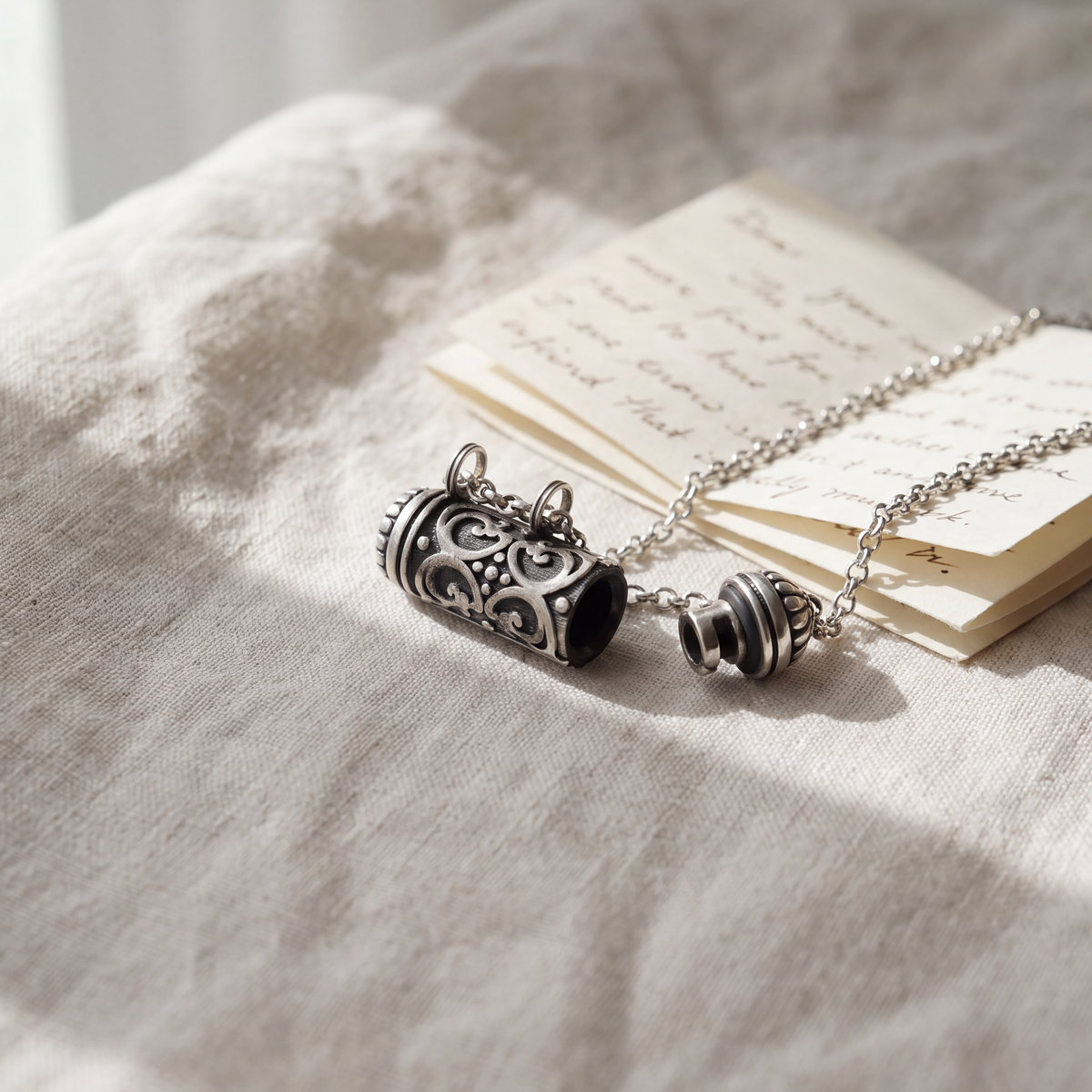 Illustrative scene of an open Sri silver amulet, its cap attached to the chain, beside a handwritten letter.