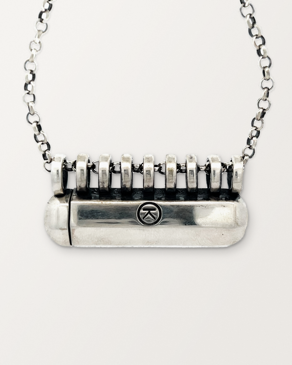 Close-up of the closed sterling silver Kerala Large amulet necklace, front, on a warm bone-white background.