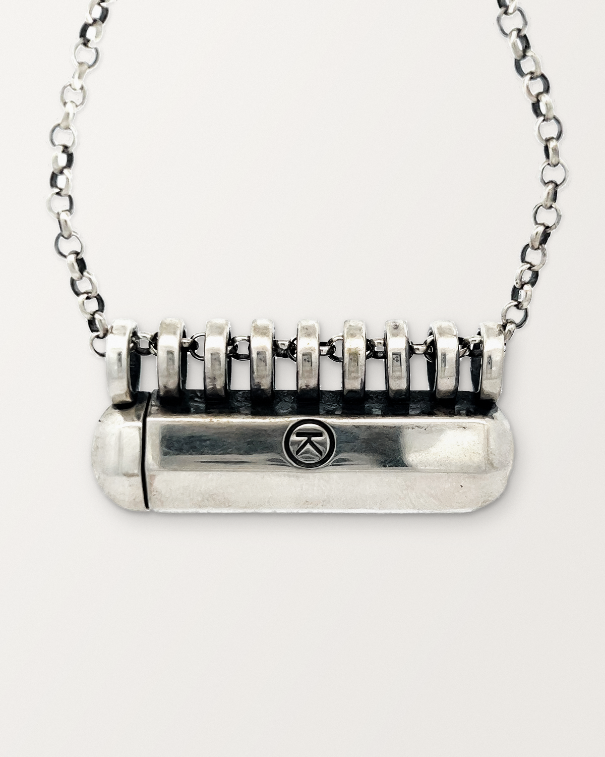 Close-up of the closed sterling silver Kerala Large amulet necklace, front, on a warm bone-white background.