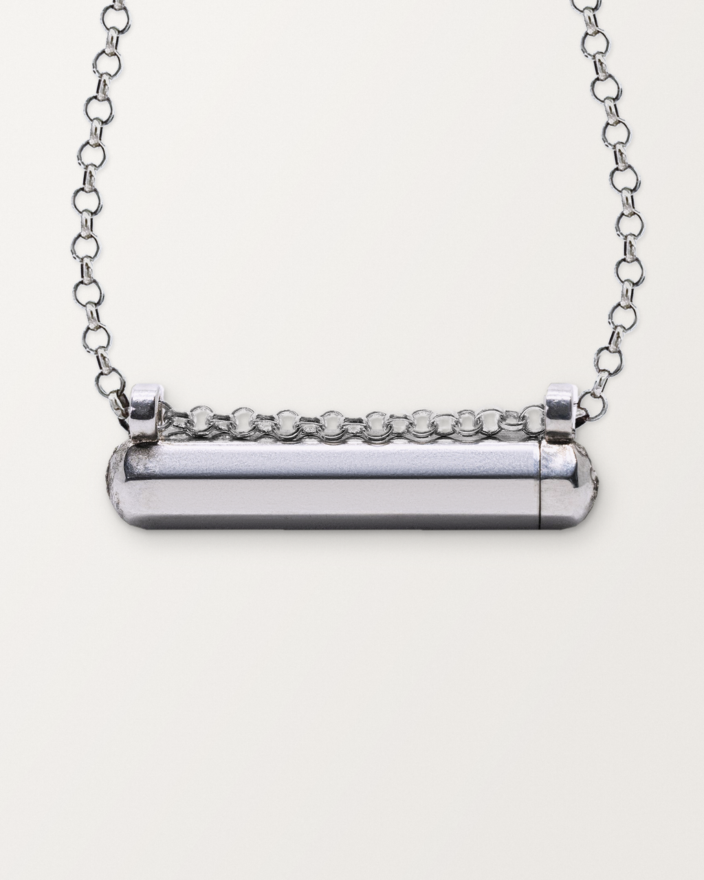 Close-up of the closed sterling silver Kerala Small amulet necklace, front, on a warm bone-white background.
