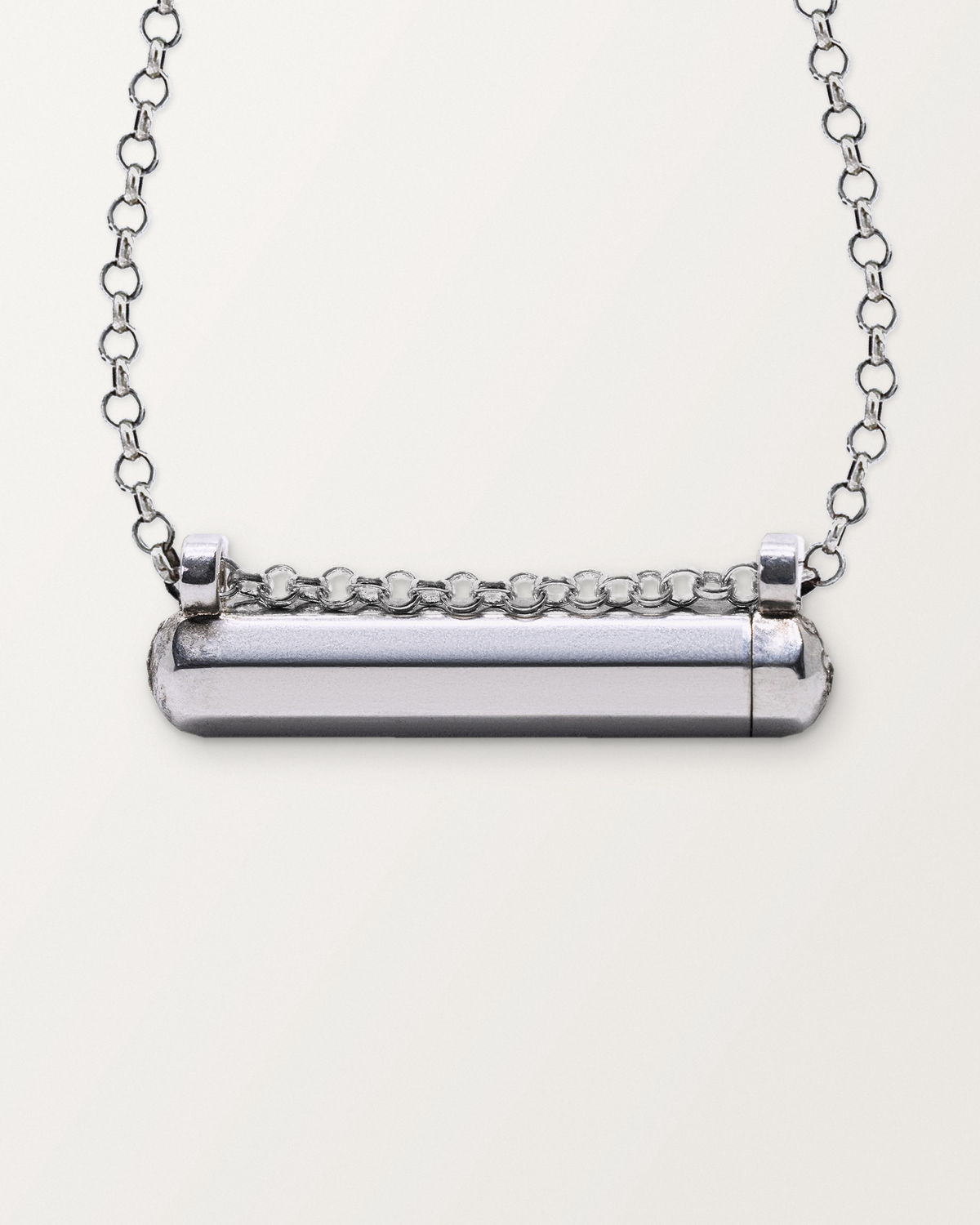 Close-up of the closed sterling silver Kerala Small amulet necklace, front, on a warm bone-white background.