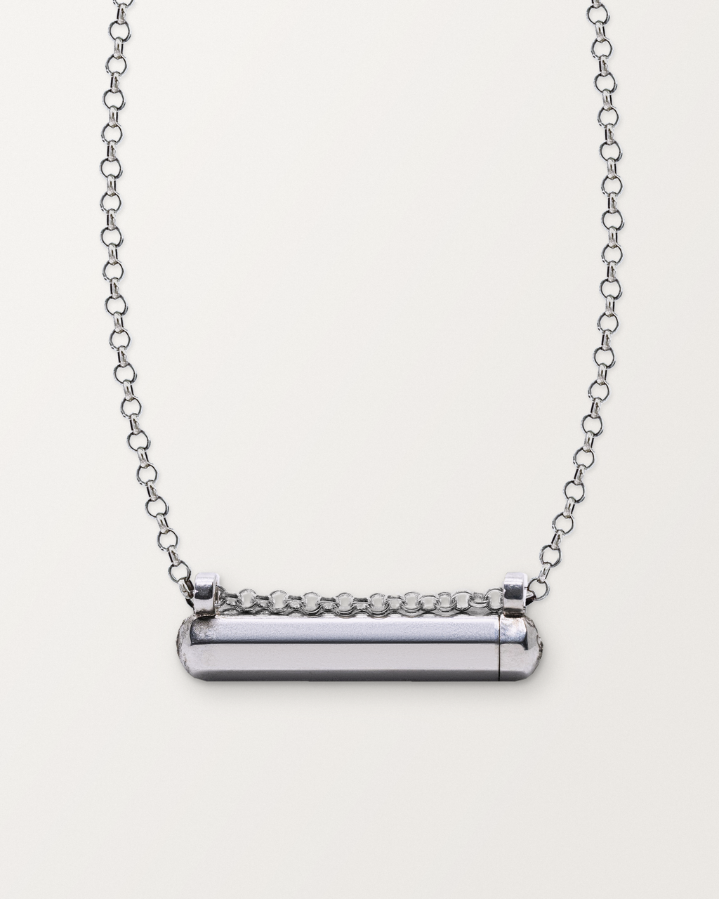 Sterling silver Kerala Small amulet necklace, closed, on a warm bone-white background, chain exiting the top of frame.