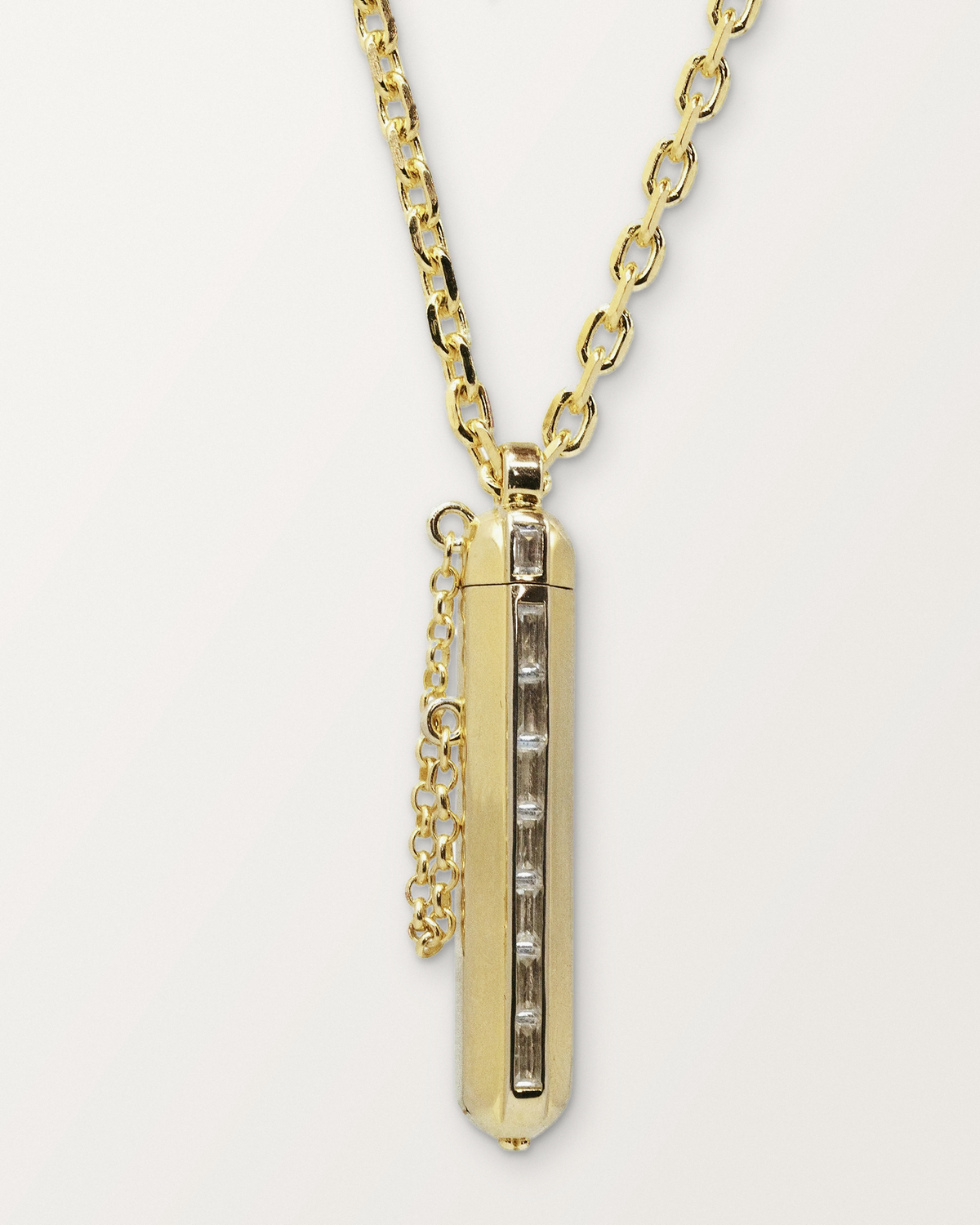 Kerala Vertical openable amulet necklace in 14K or 18K yellow gold, shown closed on a warm bone-white background.