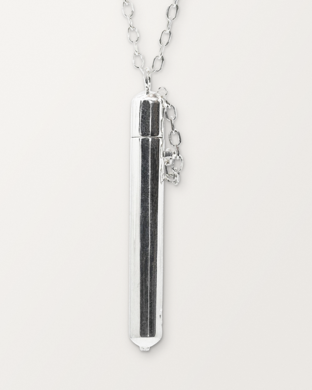 Close-up of the closed sterling silver Moksha amulet necklace, front, on a warm bone-white background.