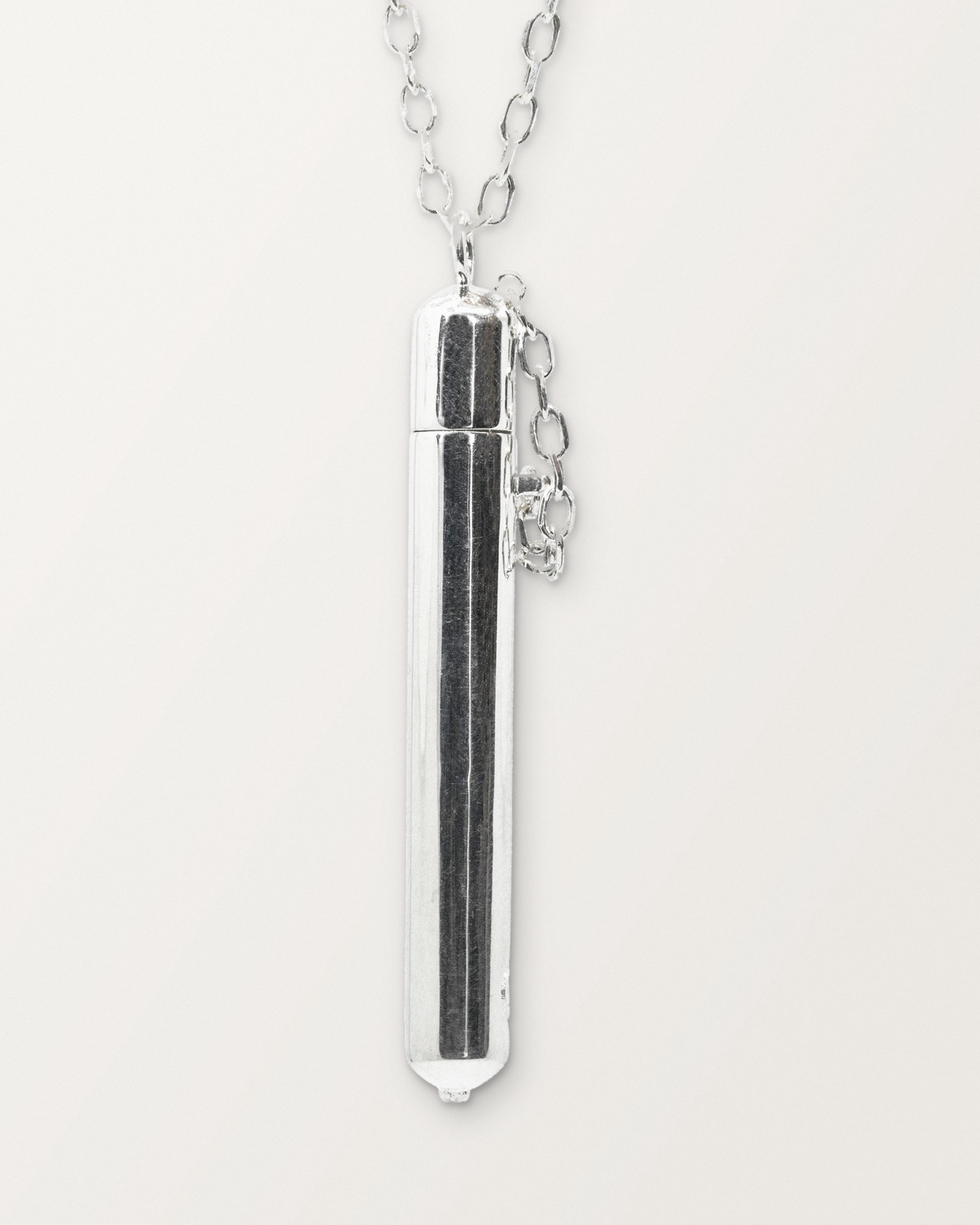 Close-up of the closed sterling silver Moksha amulet necklace, front, on a warm bone-white background.
