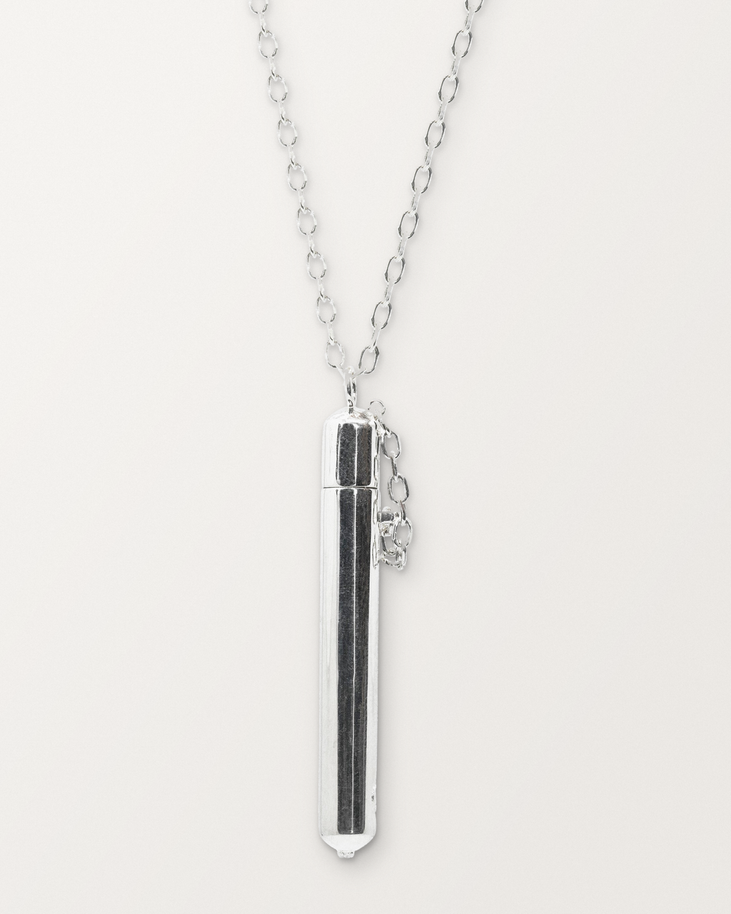 Sterling silver Moksha amulet necklace, closed, hanging on its chain against a warm bone-white background.