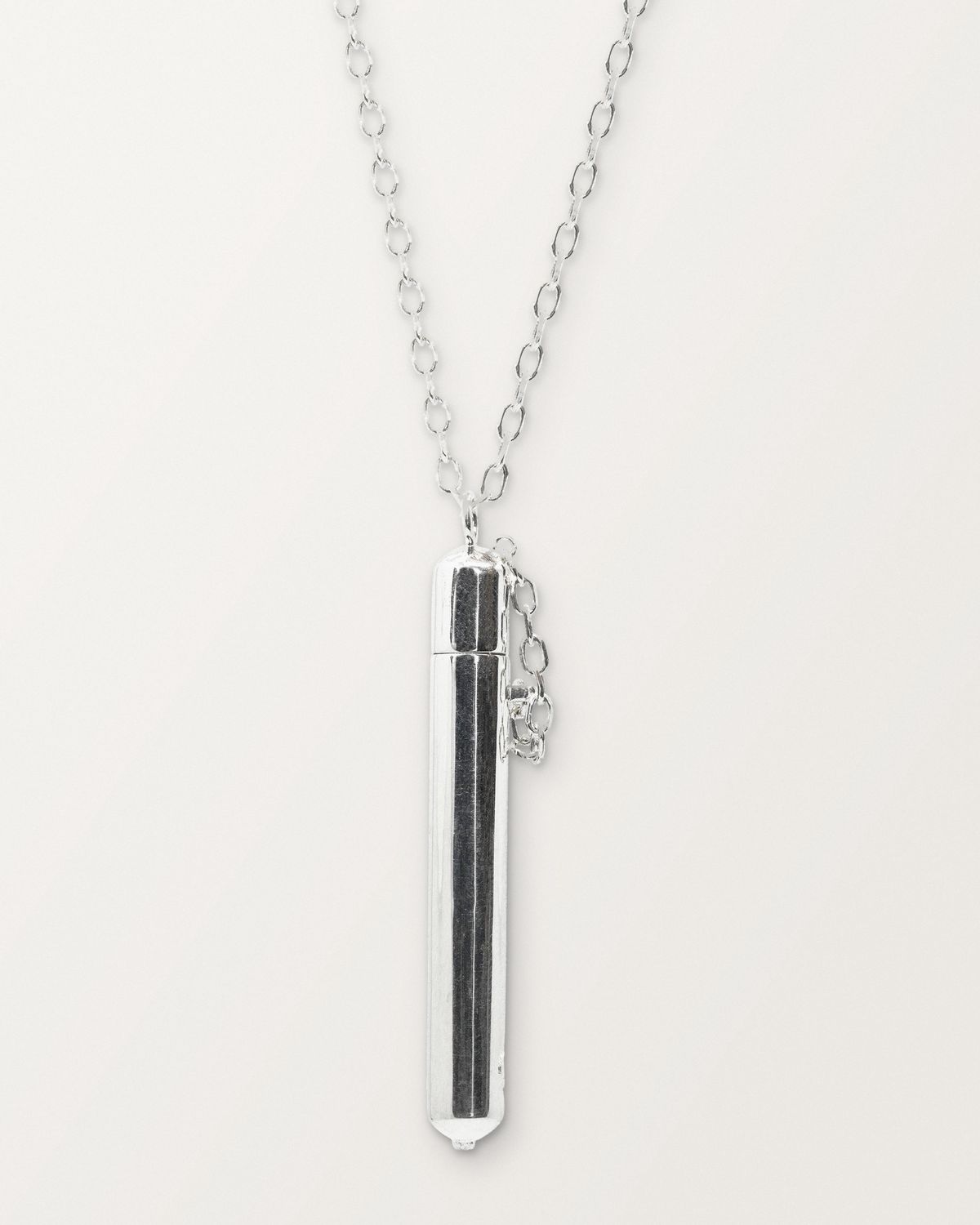 Sterling silver Moksha amulet necklace, closed, hanging on its chain against a warm bone-white background.