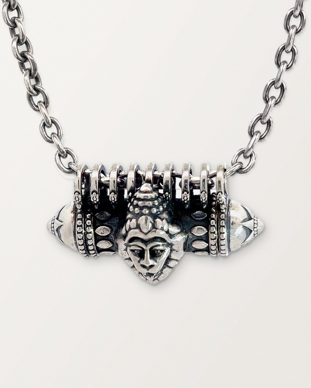 Close-up of the closed sterling silver Narashimha amulet necklace, front, on a warm bone-white background.