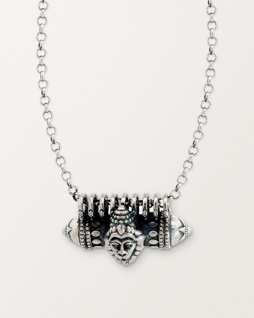 Sterling silver Narashimha amulet necklace, closed, on a warm bone-white background.