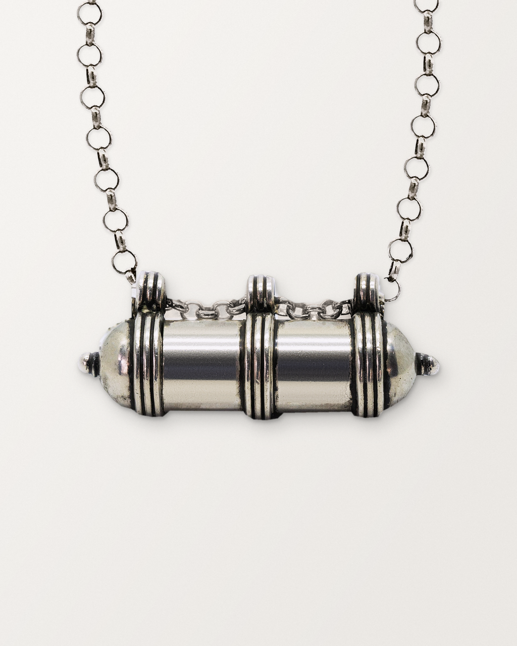 Close-up of the closed sterling silver Pankaj amulet necklace, front, on a warm bone-white background.