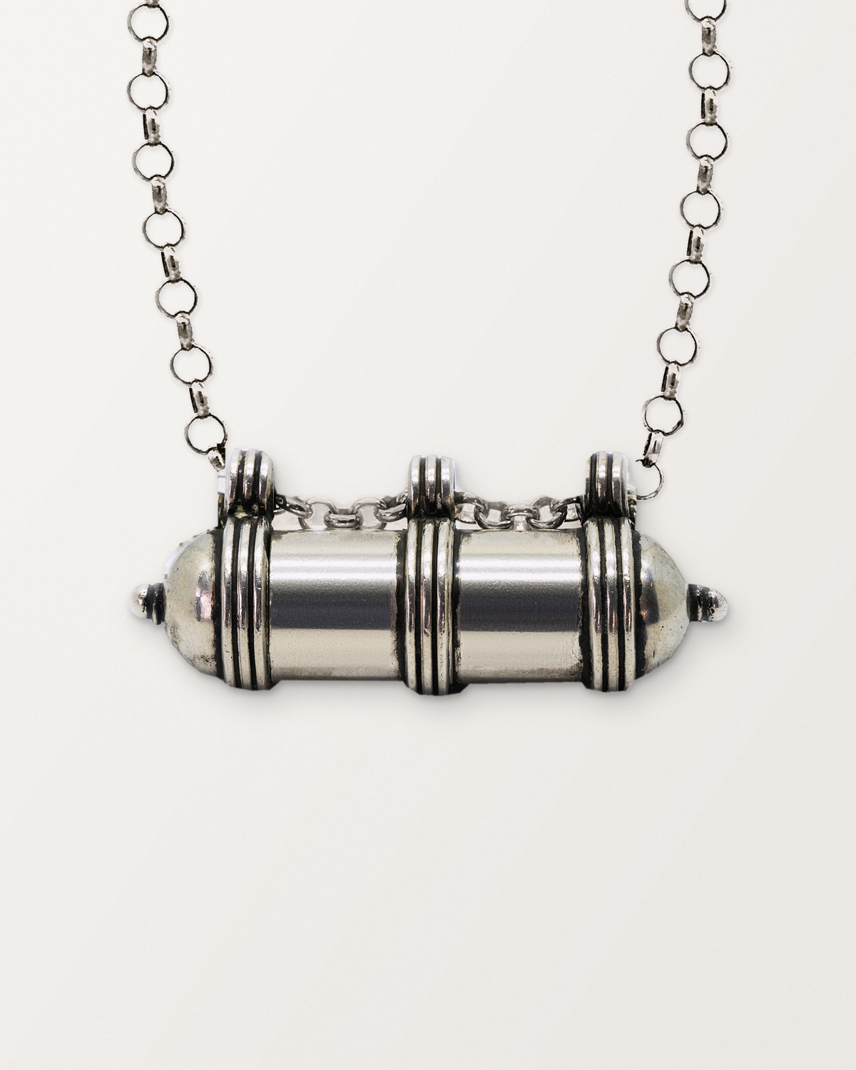 Close-up of the closed sterling silver Pankaj amulet necklace, front, on a warm bone-white background.
