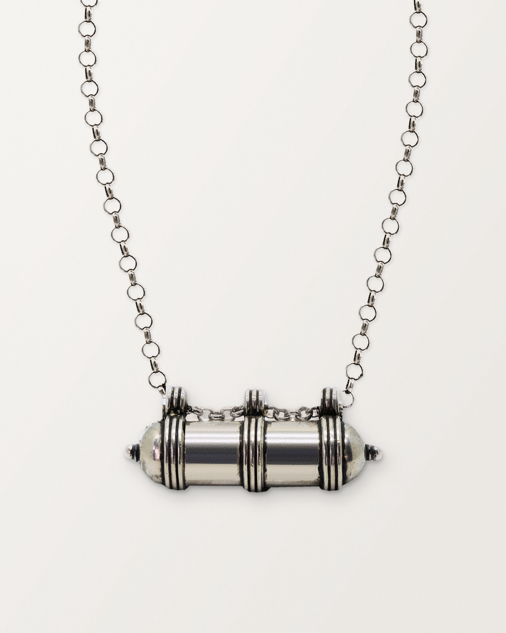 Sterling silver Pankaj amulet necklace, closed, on a warm bone-white background, chain exiting the top of frame.