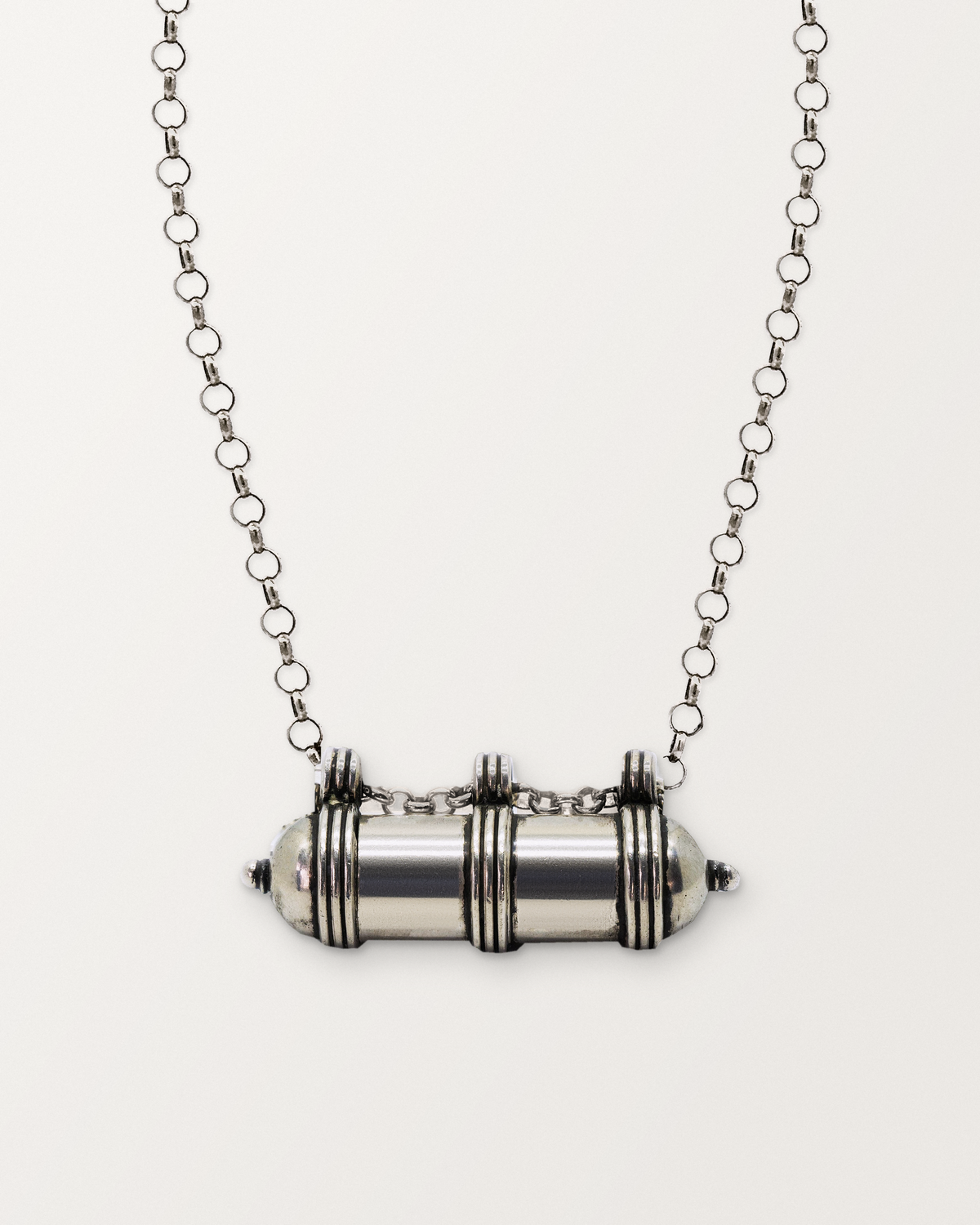 Sterling silver Pankaj amulet necklace, closed, on a warm bone-white background, chain exiting the top of frame.