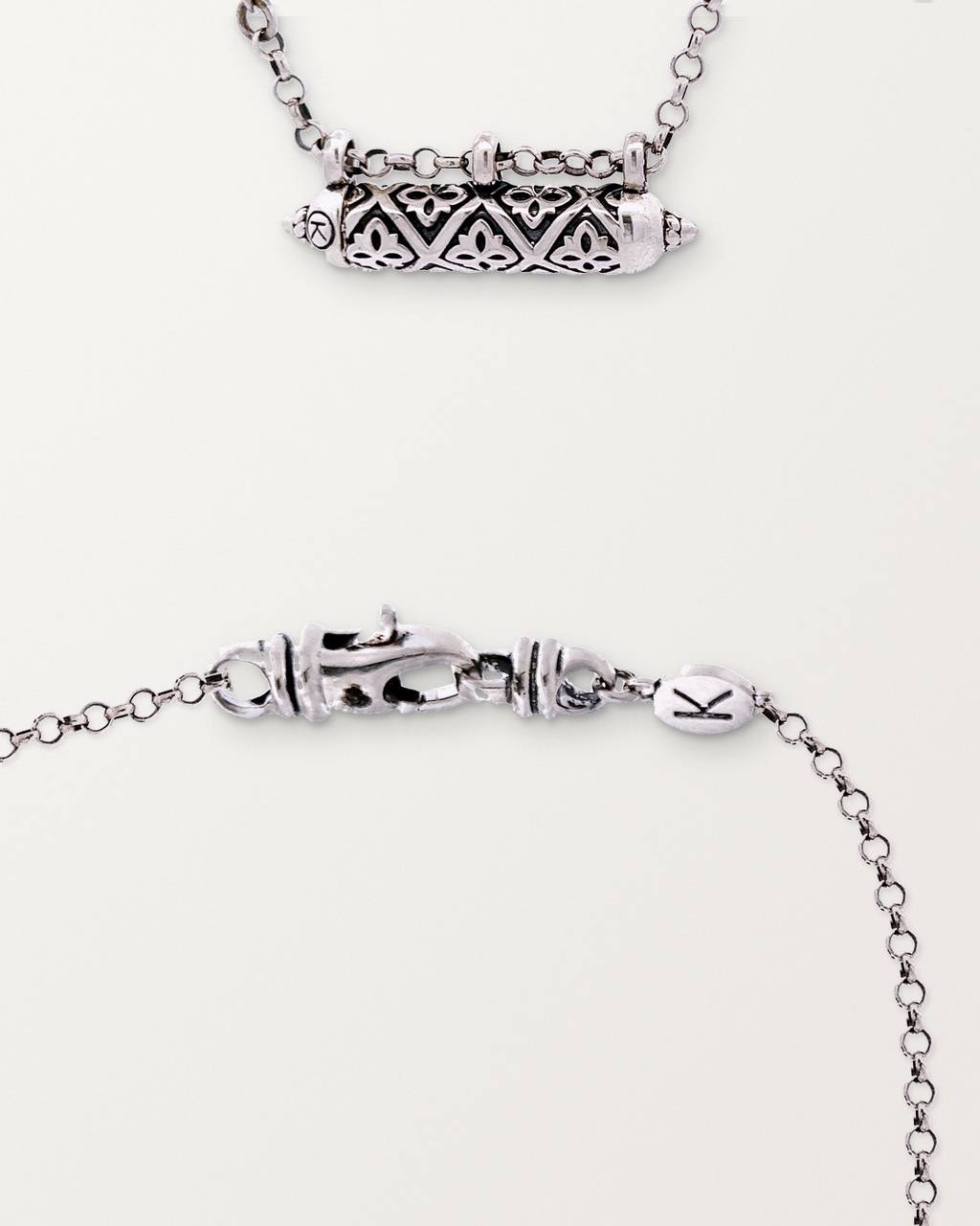 Sterling silver Shakti amulet beside a macro view of the lobster clasp and engraved oval K tag on its chain.