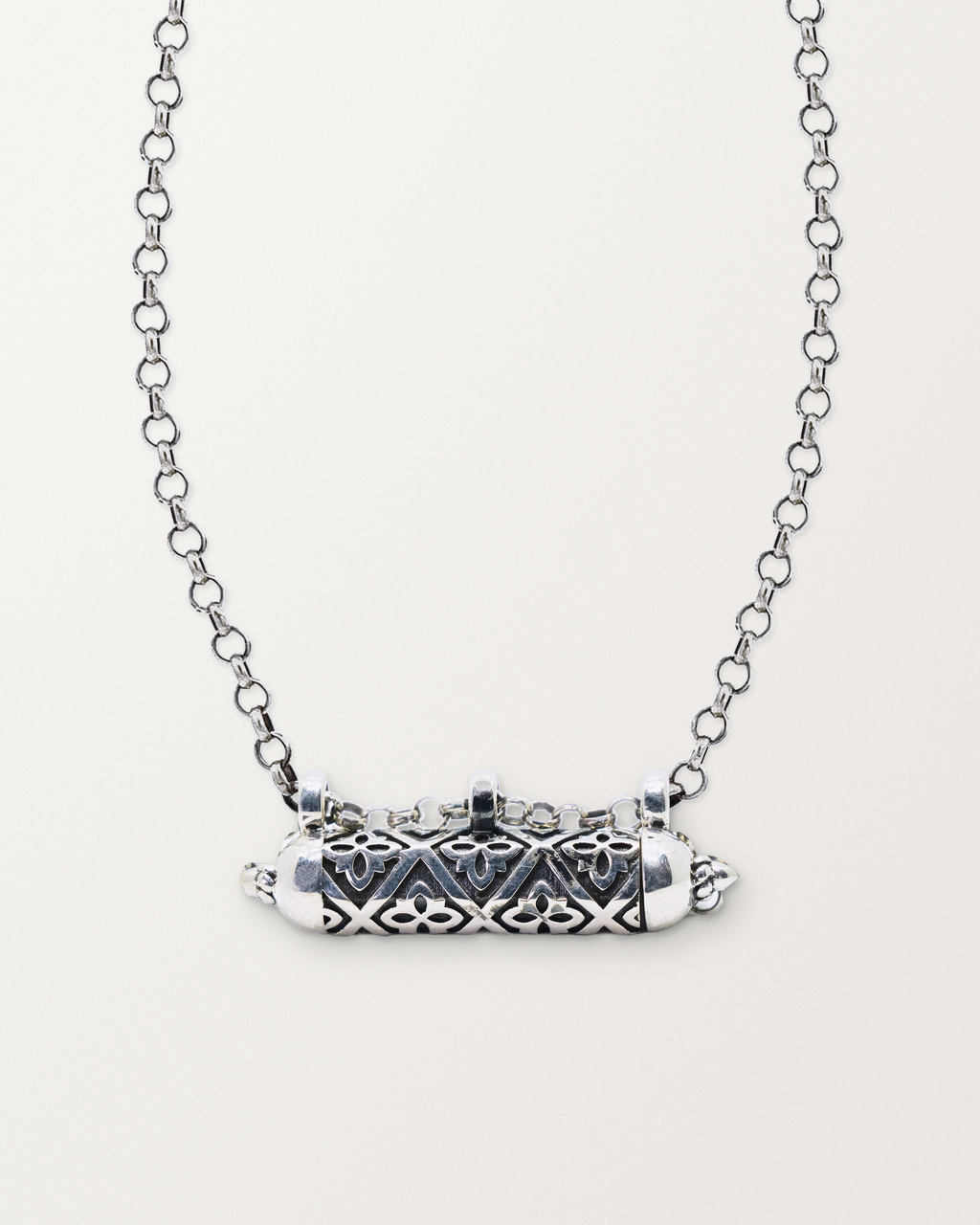 Sterling silver Shakti amulet necklace, closed, on a warm bone-white background, chain exiting the top of frame.