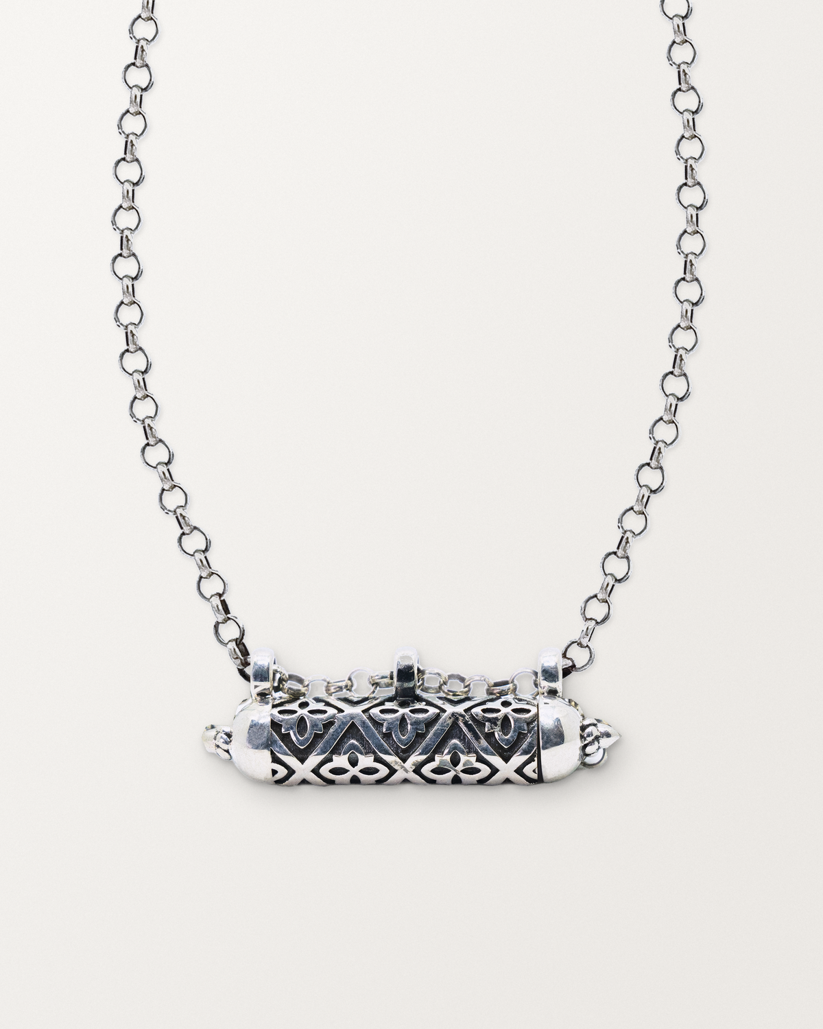 Sterling silver Shakti amulet necklace, closed, on a warm bone-white background, chain exiting the top of frame.