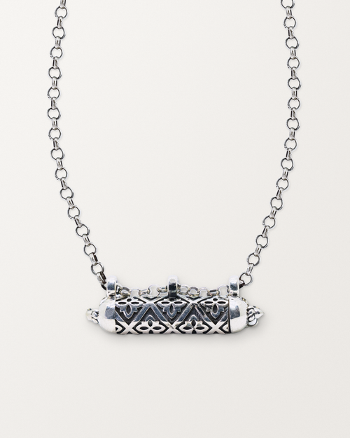 Sterling silver Shakti amulet necklace, closed, on a warm bone-white background, chain exiting the top of frame.