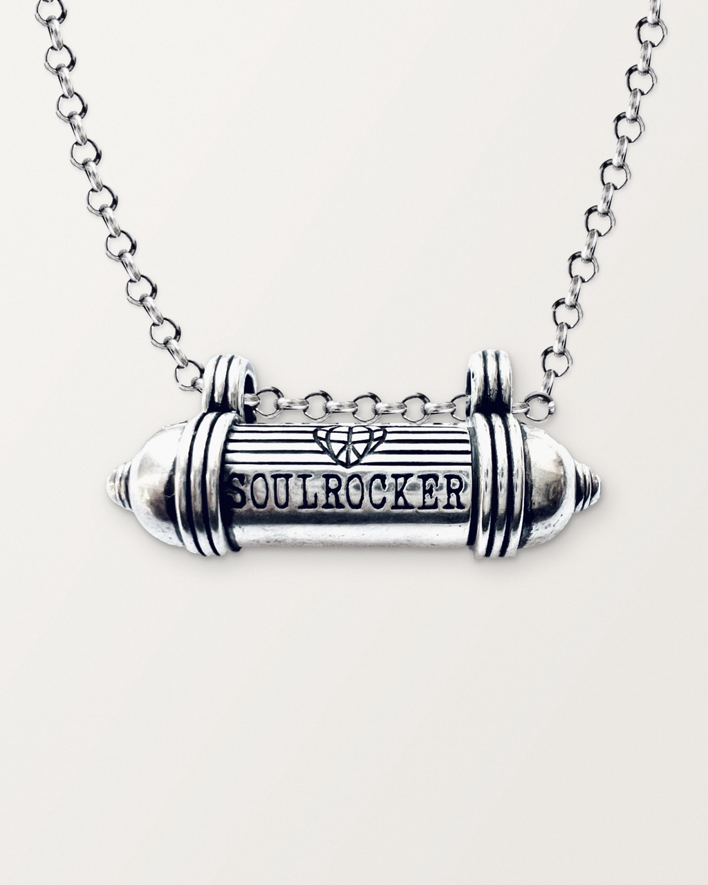 Close-up of the closed sterling silver SOULROCKER amulet necklace, engraved front, on a warm bone-white background.