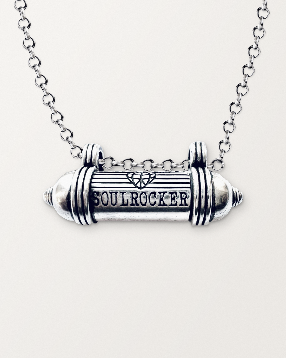 Close-up of the closed sterling silver SOULROCKER amulet necklace, engraved front, on a warm bone-white background.