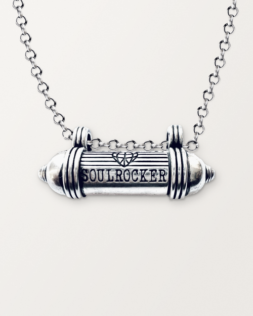 Close-up of the closed sterling silver SOULROCKER amulet necklace, engraved front, on a warm bone-white background.