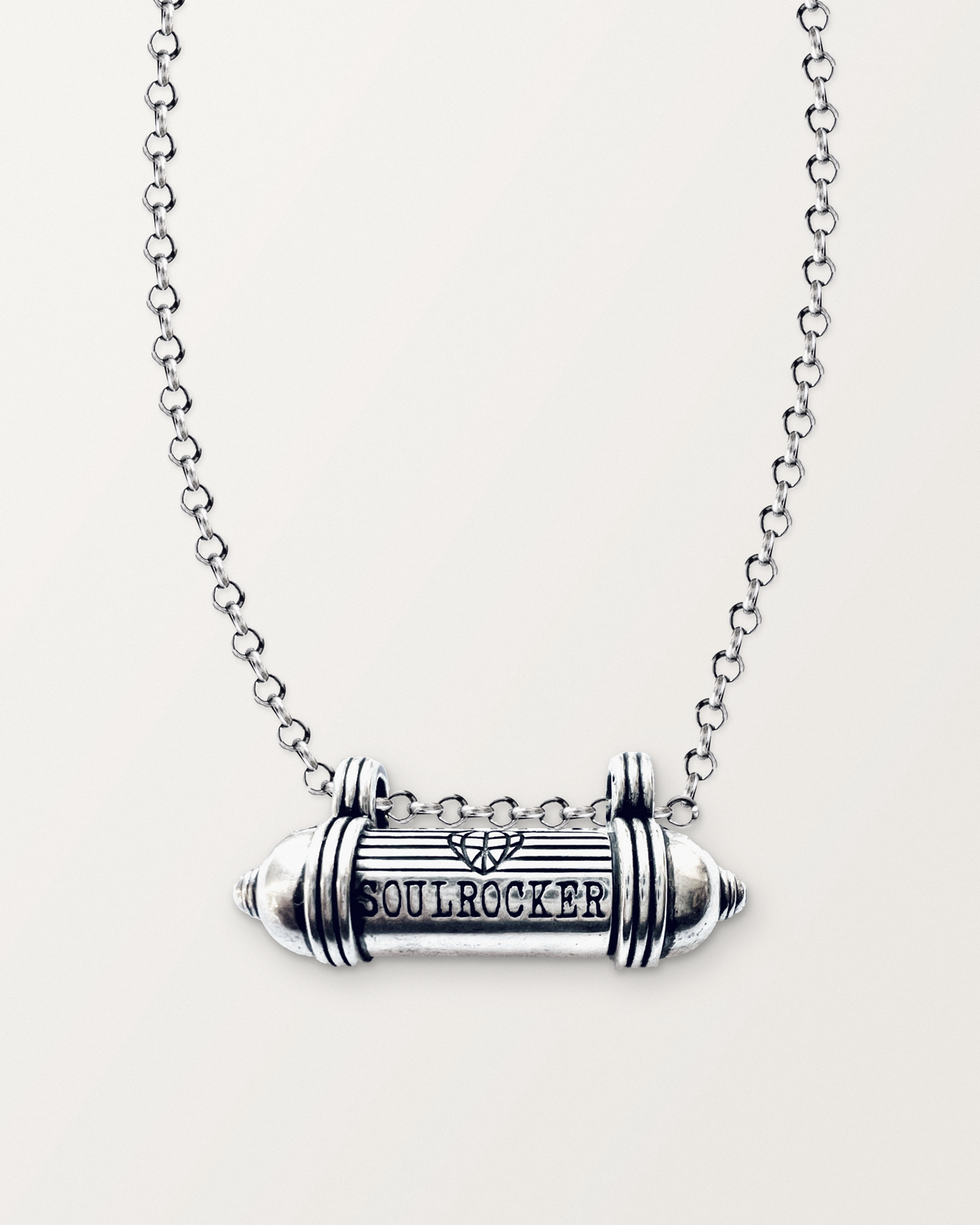 Sterling silver SOULROCKER amulet necklace, closed, engraved front, on its polished rolo chain against a warm bone-white background.
