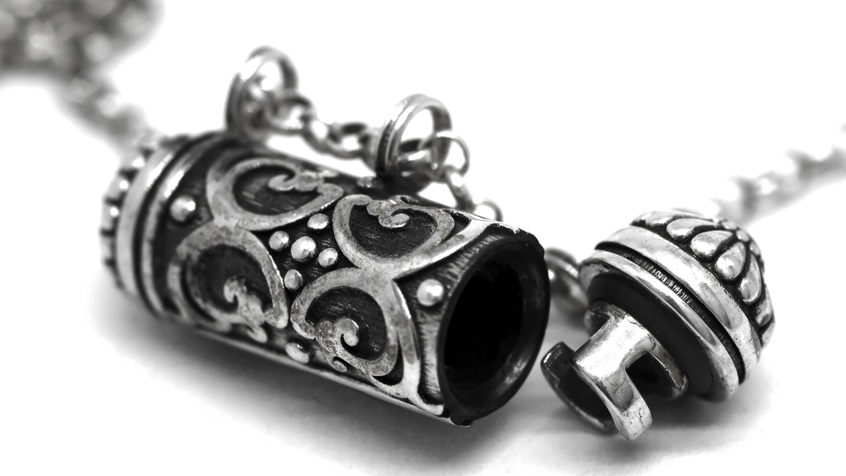 Sri sterling silver amulet open, showing the scroll relief, inner chamber, plug and gasket. Original product photograph.