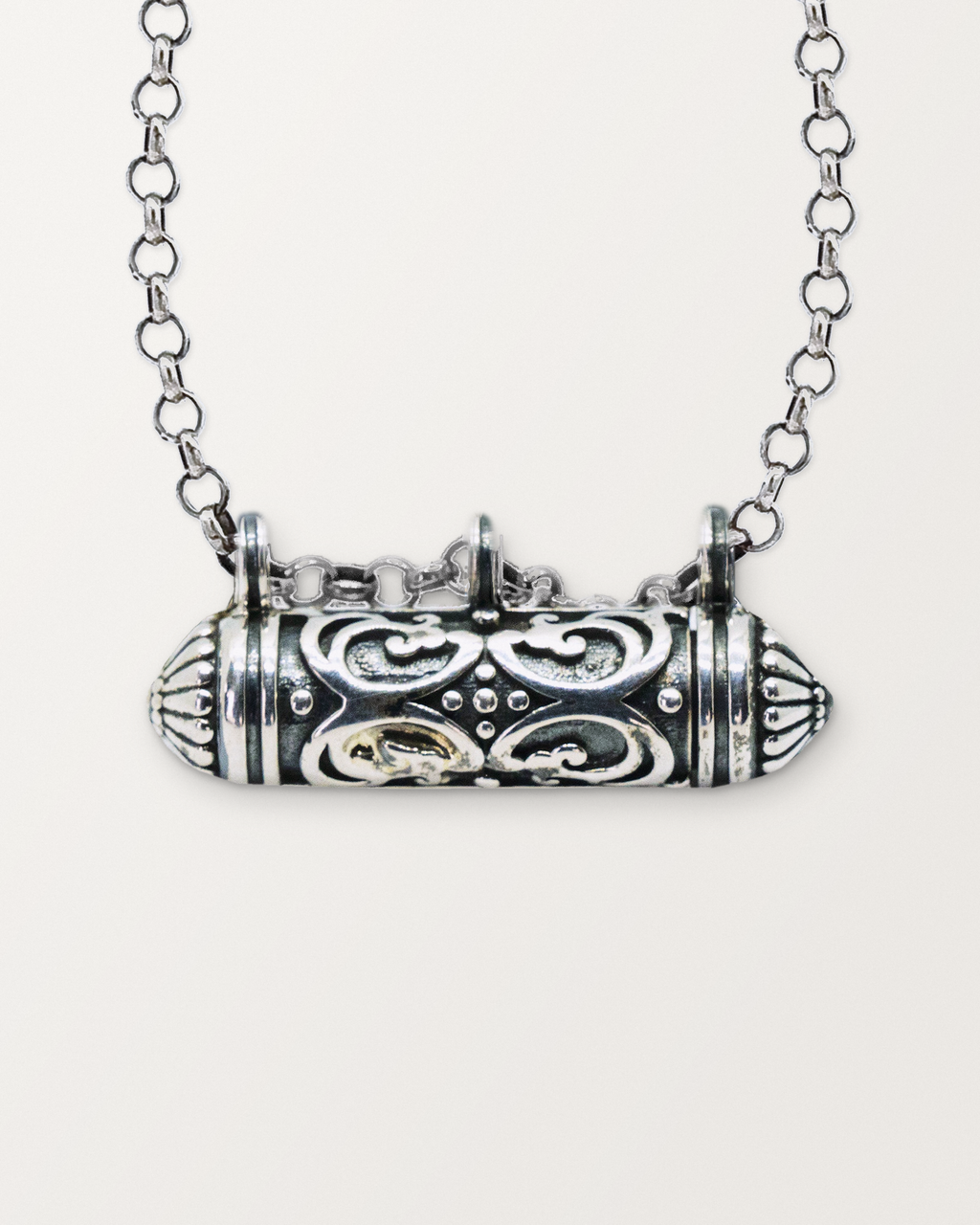 Close-up of the closed sterling silver Sri amulet necklace, front, on a warm bone-white background.