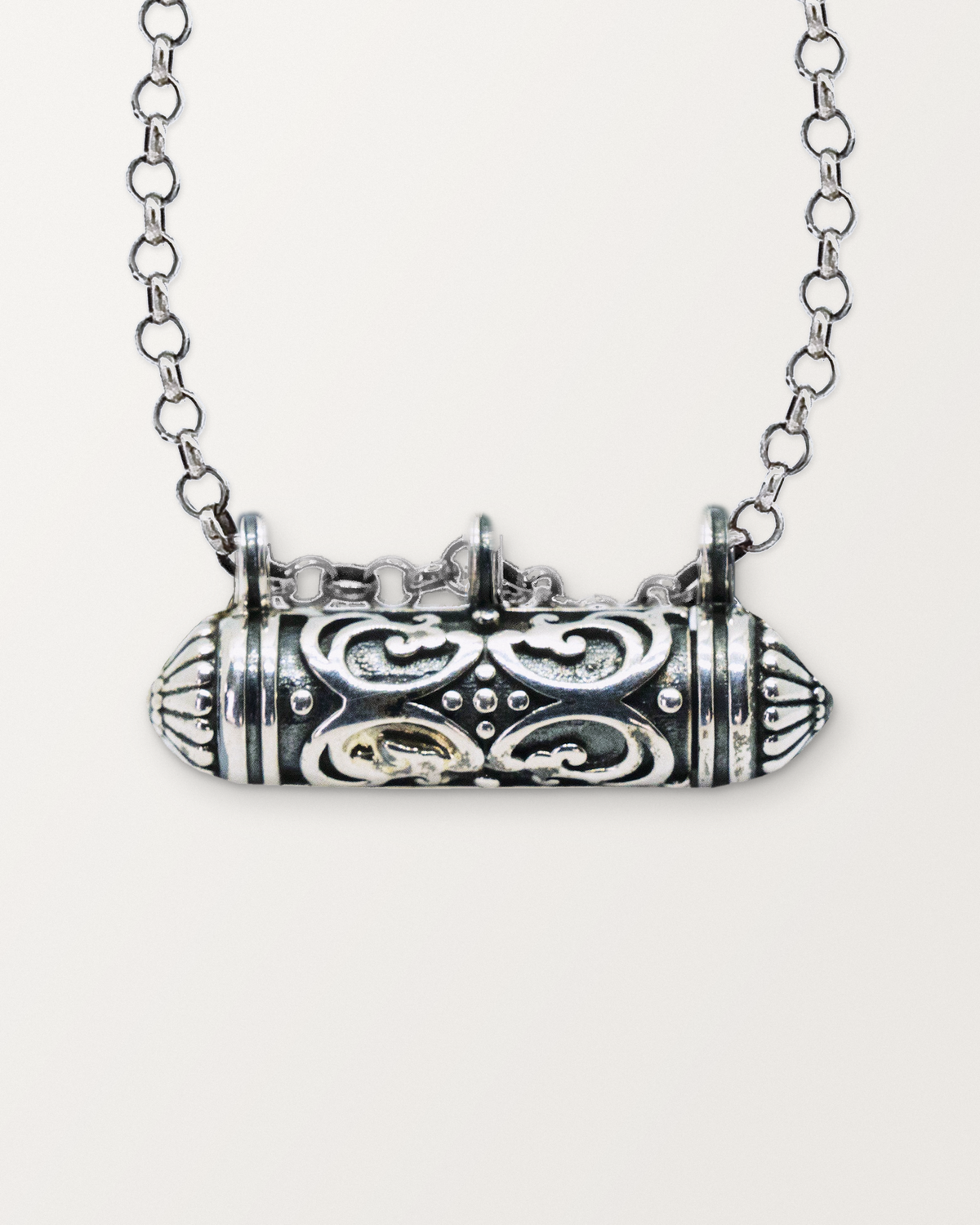 Close-up of the closed sterling silver Sri amulet necklace, front, on a warm bone-white background.