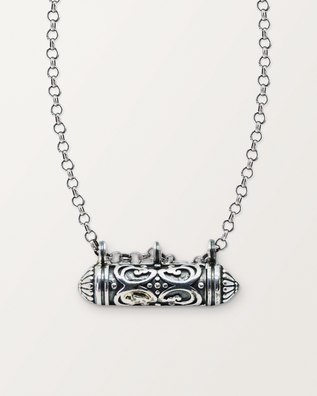 Sterling silver Sri amulet necklace, closed, on a warm bone-white background, chain exiting the top of frame.