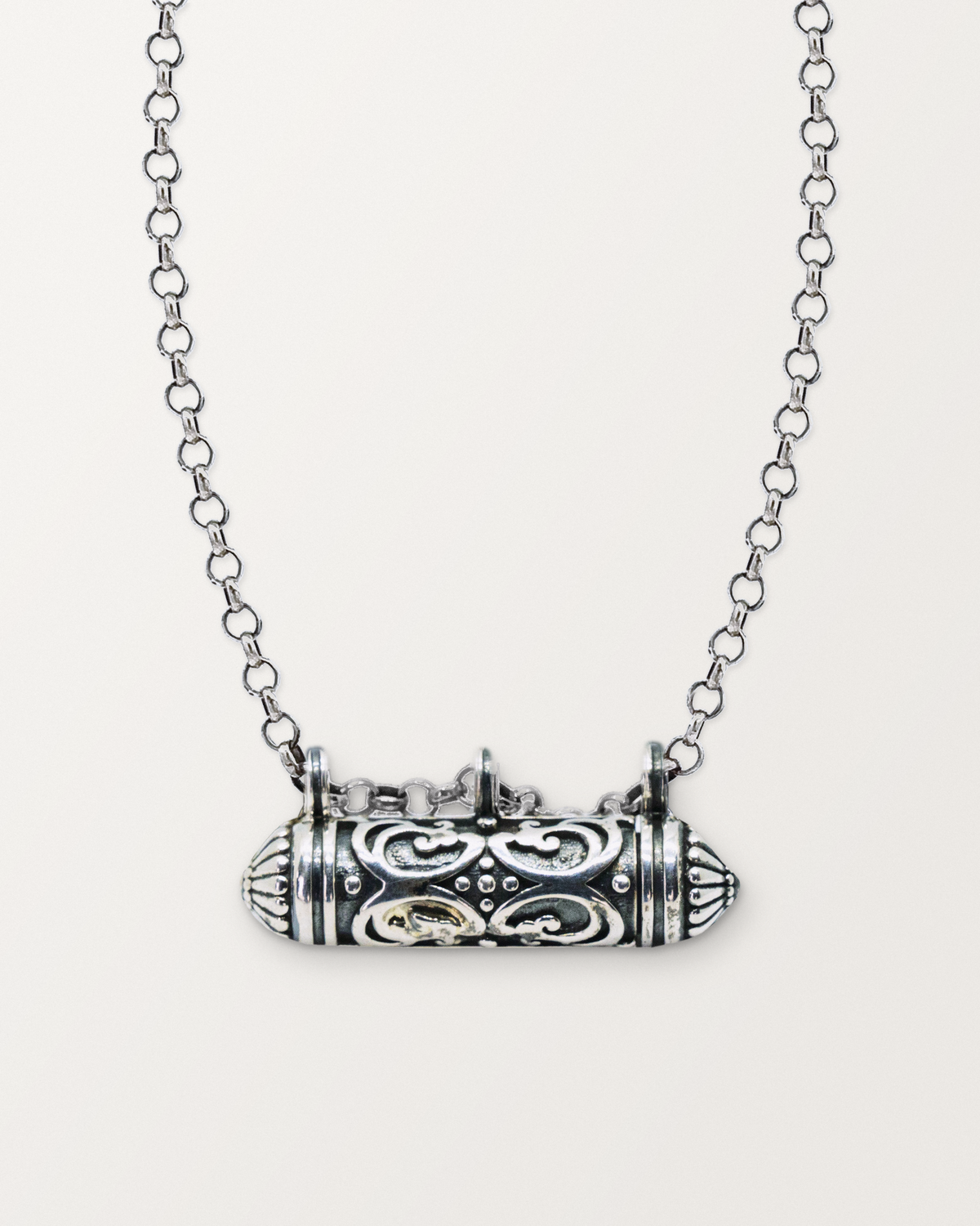 Sterling silver Sri amulet necklace, closed, on a warm bone-white background, chain exiting the top of frame.