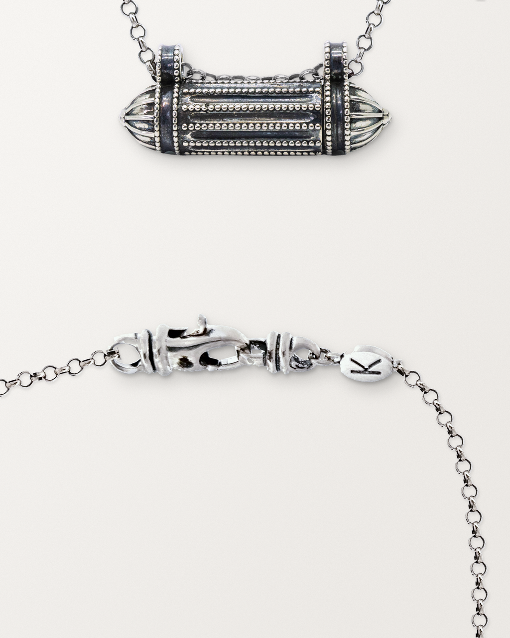 Sterling silver Taweez amulet beside a close view of the lobster clasp and oval K tag on its chain.