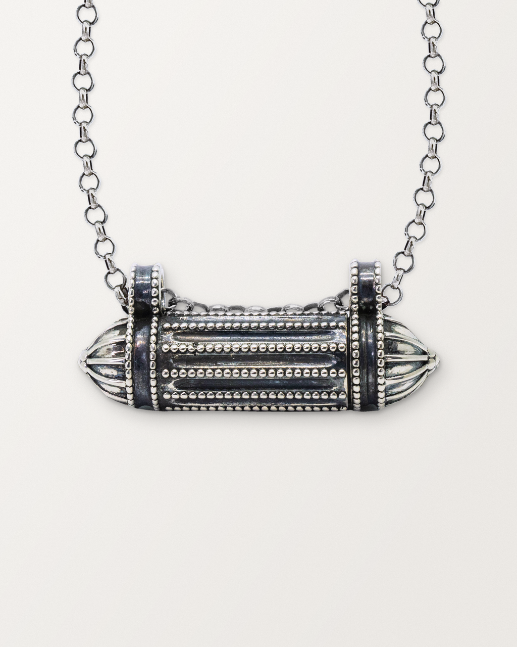 Close-up of the closed sterling silver Taweez amulet necklace, front, on a warm bone-white background.