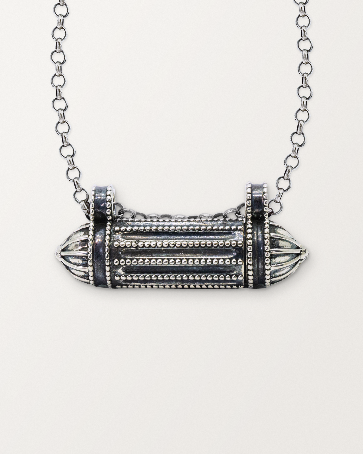 Close-up of the closed sterling silver Taweez amulet necklace, front, on a warm bone-white background.