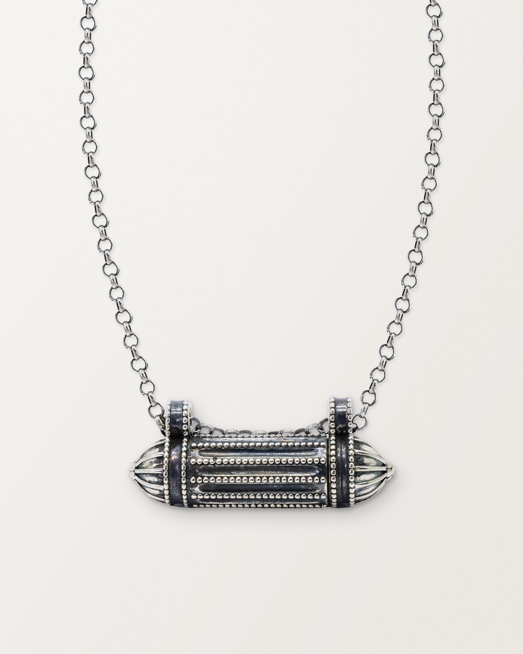 Sterling silver Taweez amulet necklace, closed, on a warm bone-white background, chain exiting the top of frame.