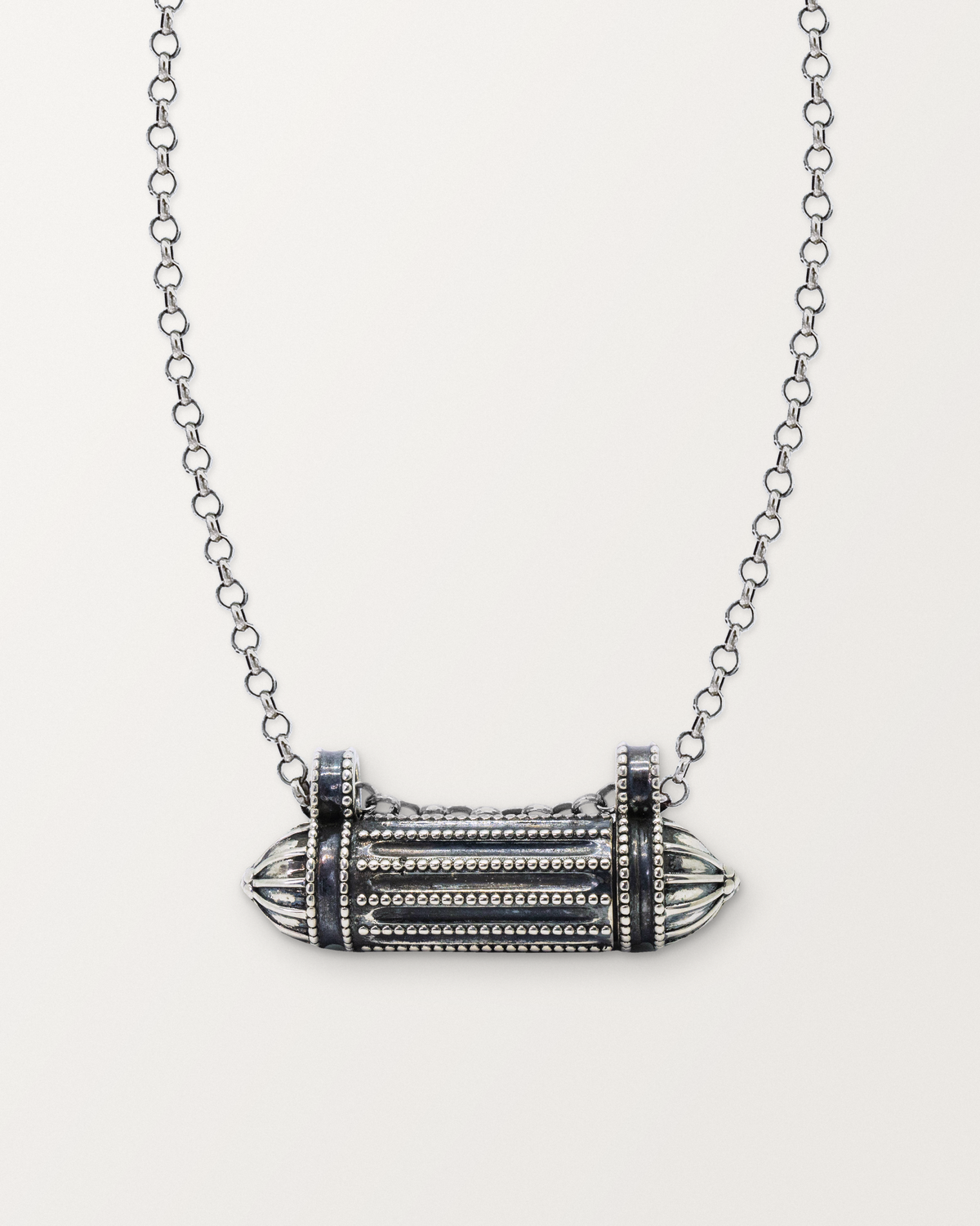 Sterling silver Taweez amulet necklace, closed, on a warm bone-white background, chain exiting the top of frame.
