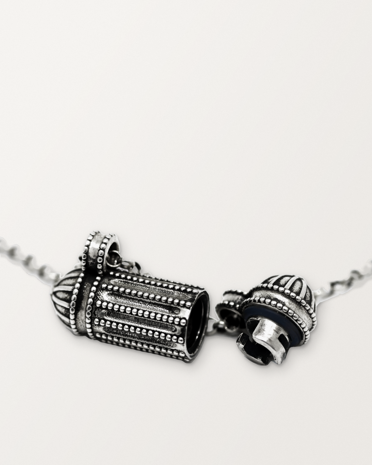 Sterling silver Taweez amulet necklace open, showing the chamber, with the cap beside it hanging on its chain by its bail.