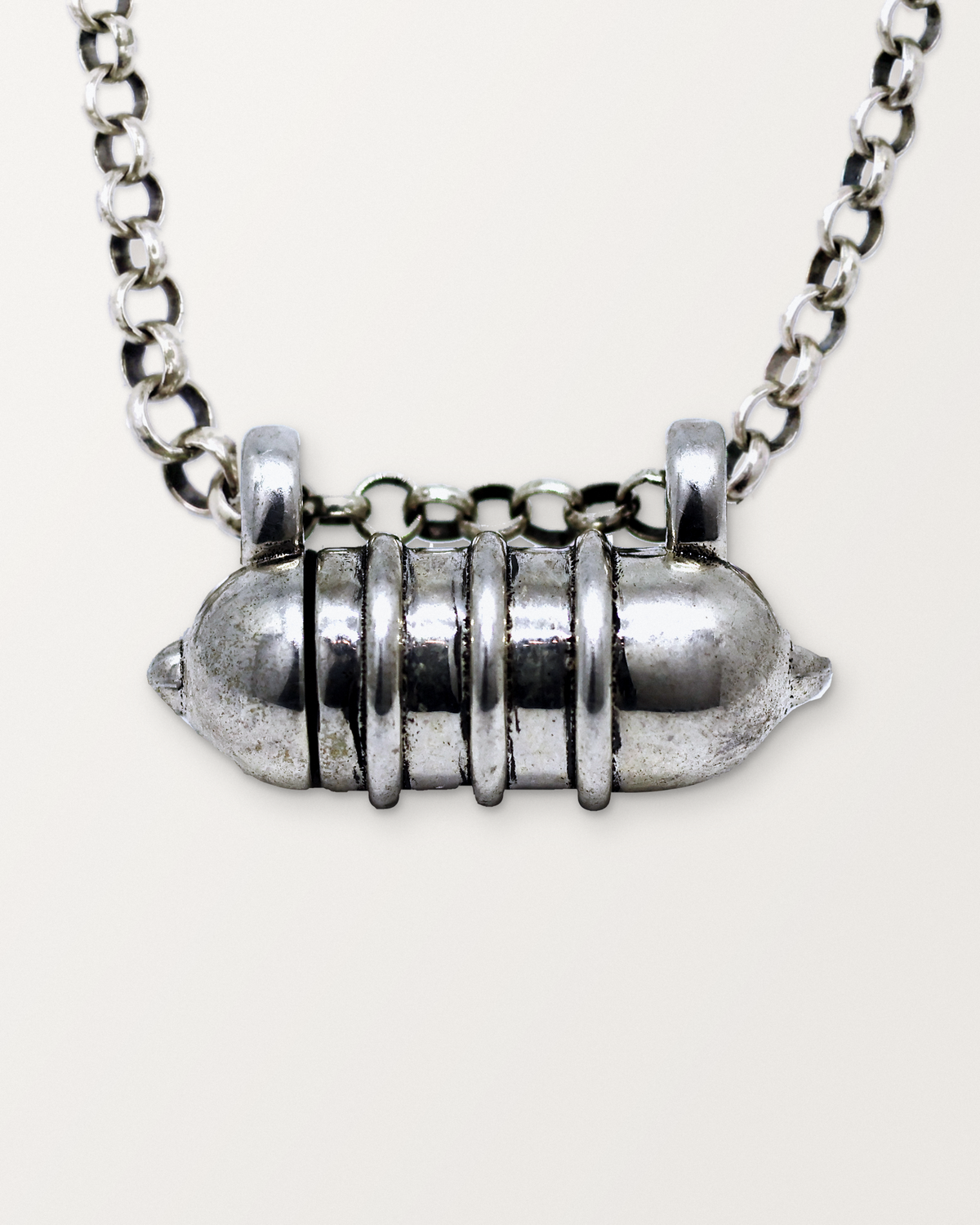 Close-up of the closed sterling silver Vámana amulet necklace, front, on a warm bone-white background.