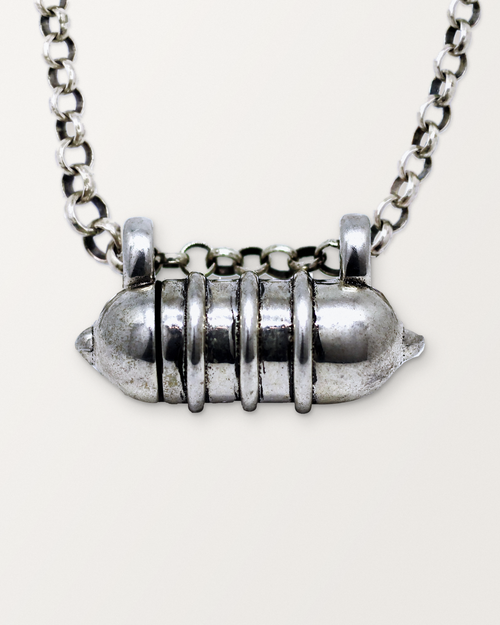 Close-up of the closed sterling silver Vámana amulet necklace, front, on a warm bone-white background.