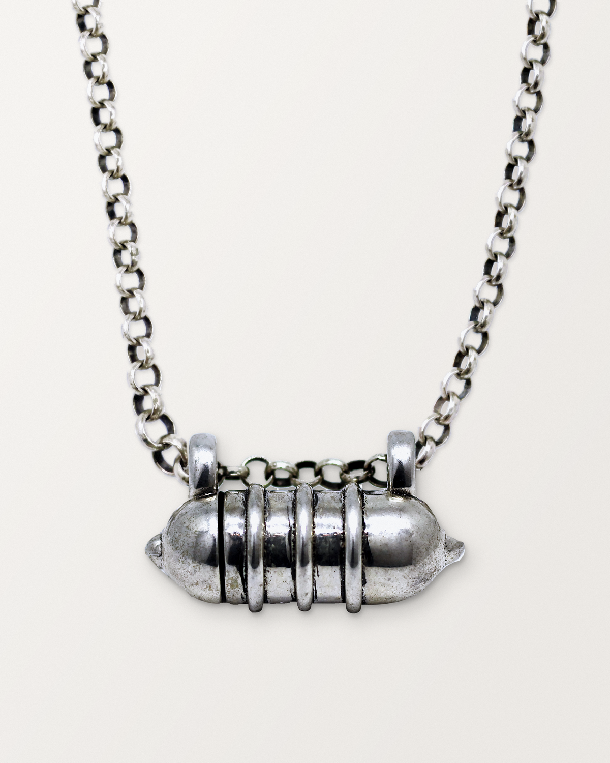 Sterling silver Vámana amulet necklace, closed, hanging on its chain against a warm bone-white background.