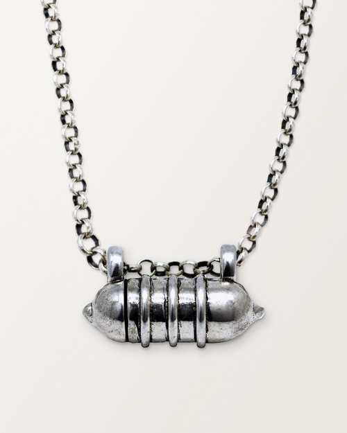 Sterling silver Vámana amulet necklace, closed, hanging on its chain against a warm bone-white background.