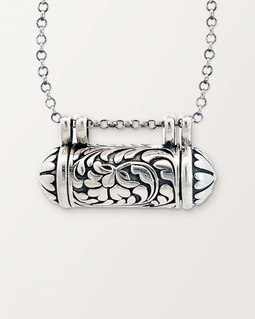 Close-up of the closed sterling silver Vana amulet necklace, front, on a warm bone-white background.