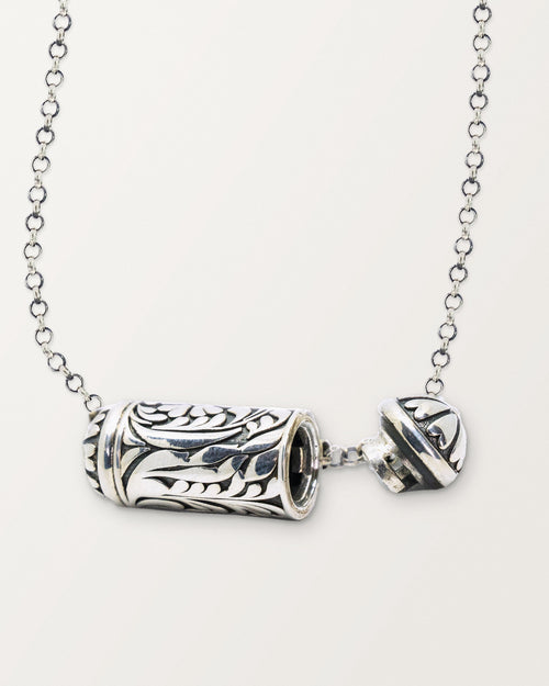 Sterling silver Vana amulet necklace, open, with its chamber visible, on a warm bone-white background.