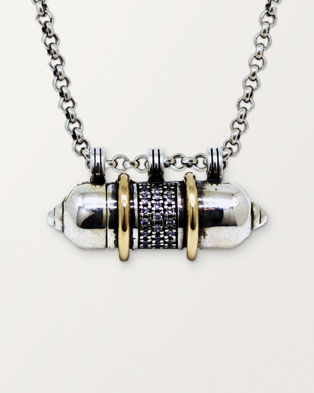 Close-up of the closed sterling silver Vidya amulet necklace with 14K yellow gold bands, front, on a warm bone-white background.